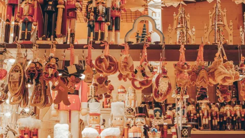 Weihnachtsmarktstand mit zahlreichen Holz-Nussknackern und verschiedenen hängenden Weihnachtsornamenten wie Brezeln, Figuren und Dekorationen in warmem, festlichem Licht. Foto © Unsplash.