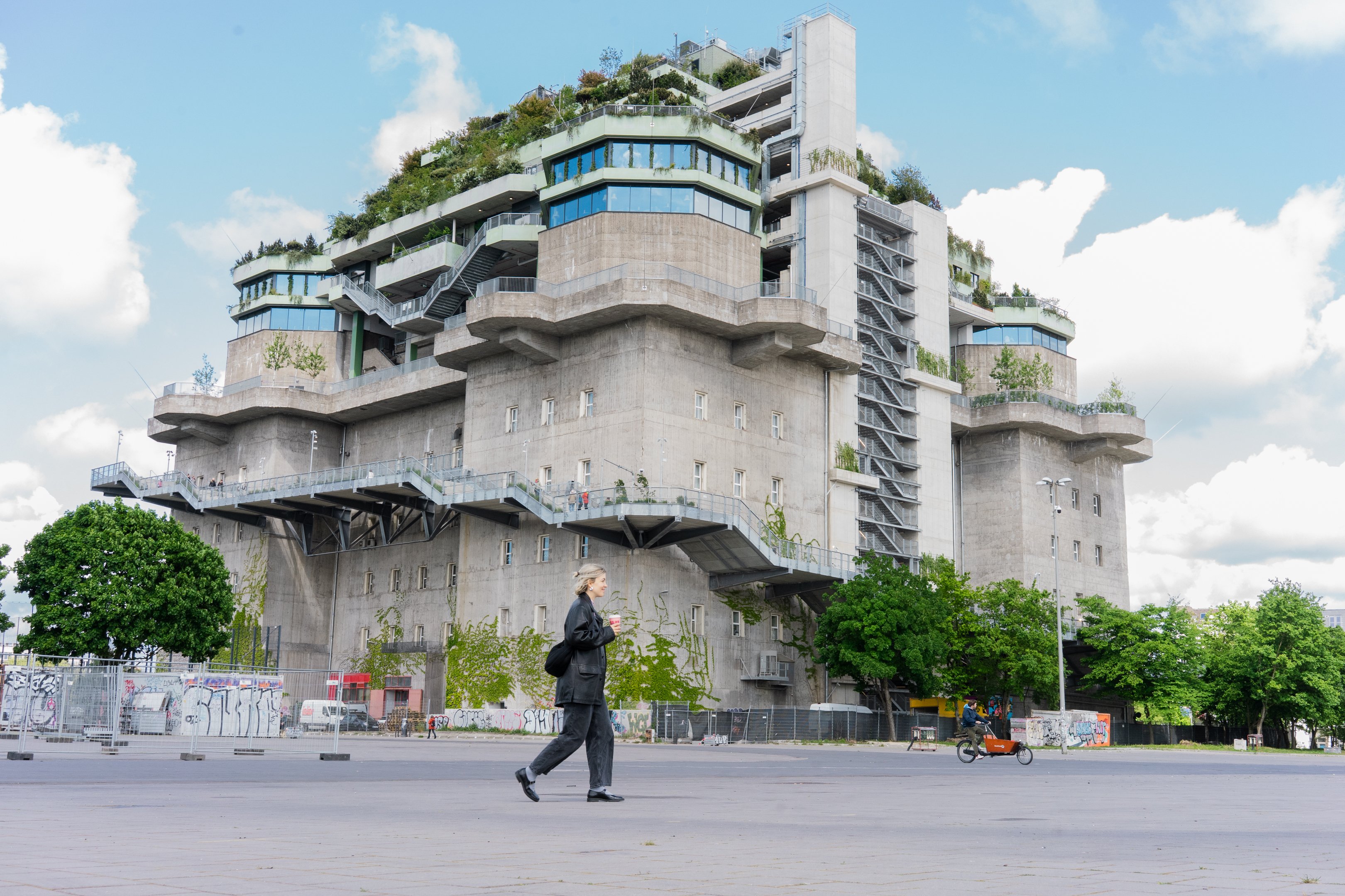 Der Bunker von Hamburg mit grünem Dach und einem Weg, welcher ausserhalb hinaufführt, während eine Person im Vordergrund durch das Bild läuft.