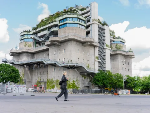 Der Bunker von Hamburg mit grünem Dach und einem Weg, welcher ausserhalb hinaufführt, während eine Person im Vordergrund durch das Bild läuft.