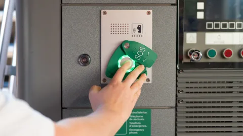 L’index d’une personne appuie sur le bouton vert «SOS» dans le train.