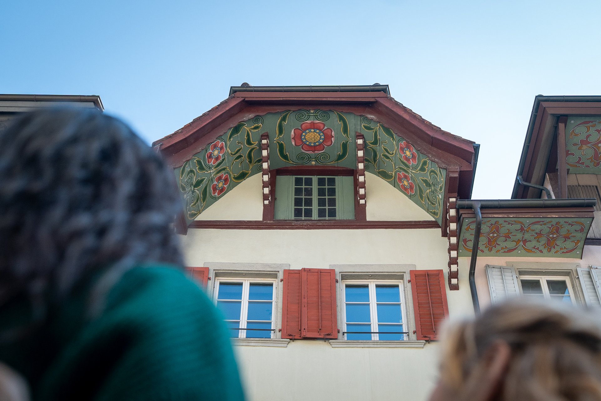 Über die Schulter einer Frau sieht man ein mit Blumen bemalter Dachgiebel.
