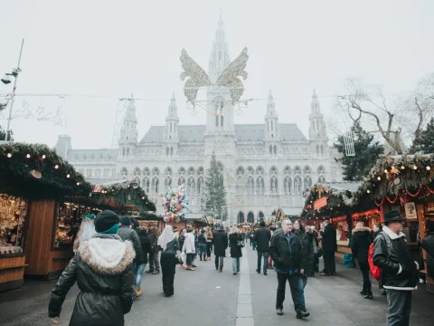 Menschen spazieren über einen festlich beleuchteten Weihnachtsmarkt mit bunten Ständen und winterlicher Atmosphäre.