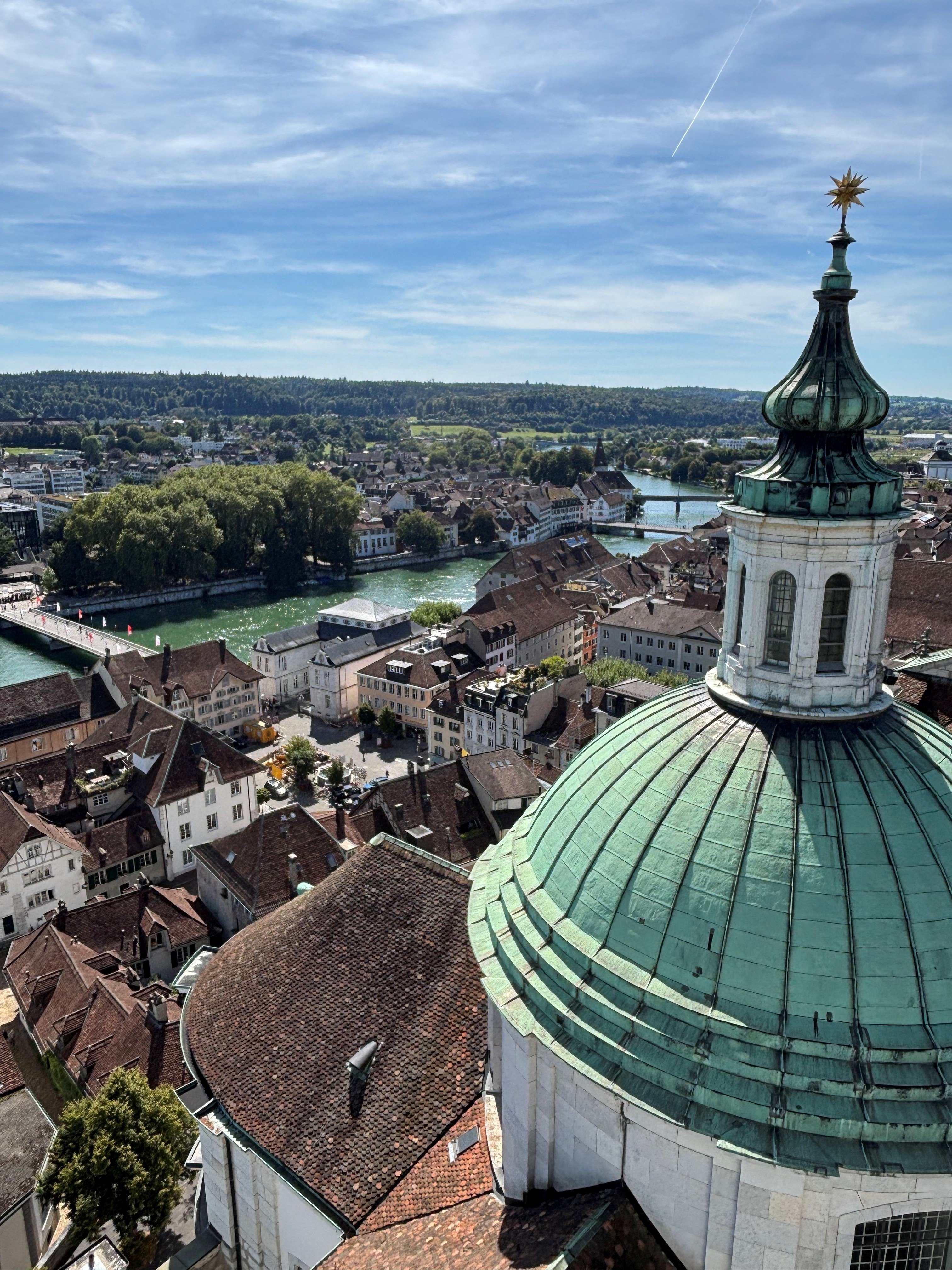 Eine Stadt, durch die ein Fluss fliesst, von oben gesehen. Im Vordergrund befindet sich ein Turm mit einem grünlichen, kuppelförmigen Dach.