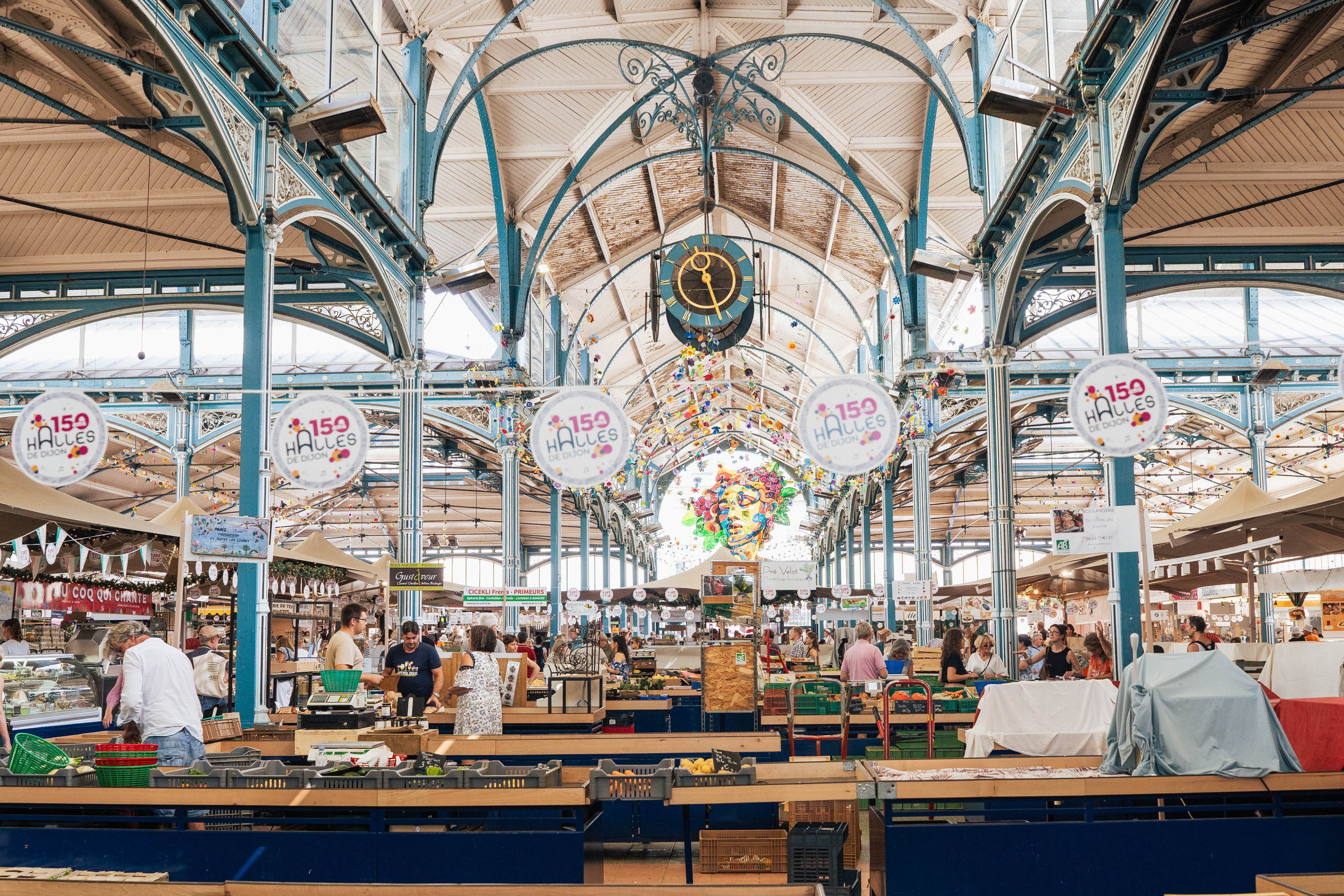 Padiglioni del mercato con strutture metalliche blu, un orologio e le bancarelle. 