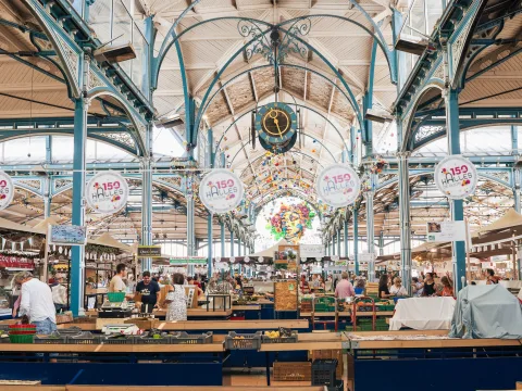 Padiglioni del mercato con strutture metalliche blu, un orologio e le bancarelle.