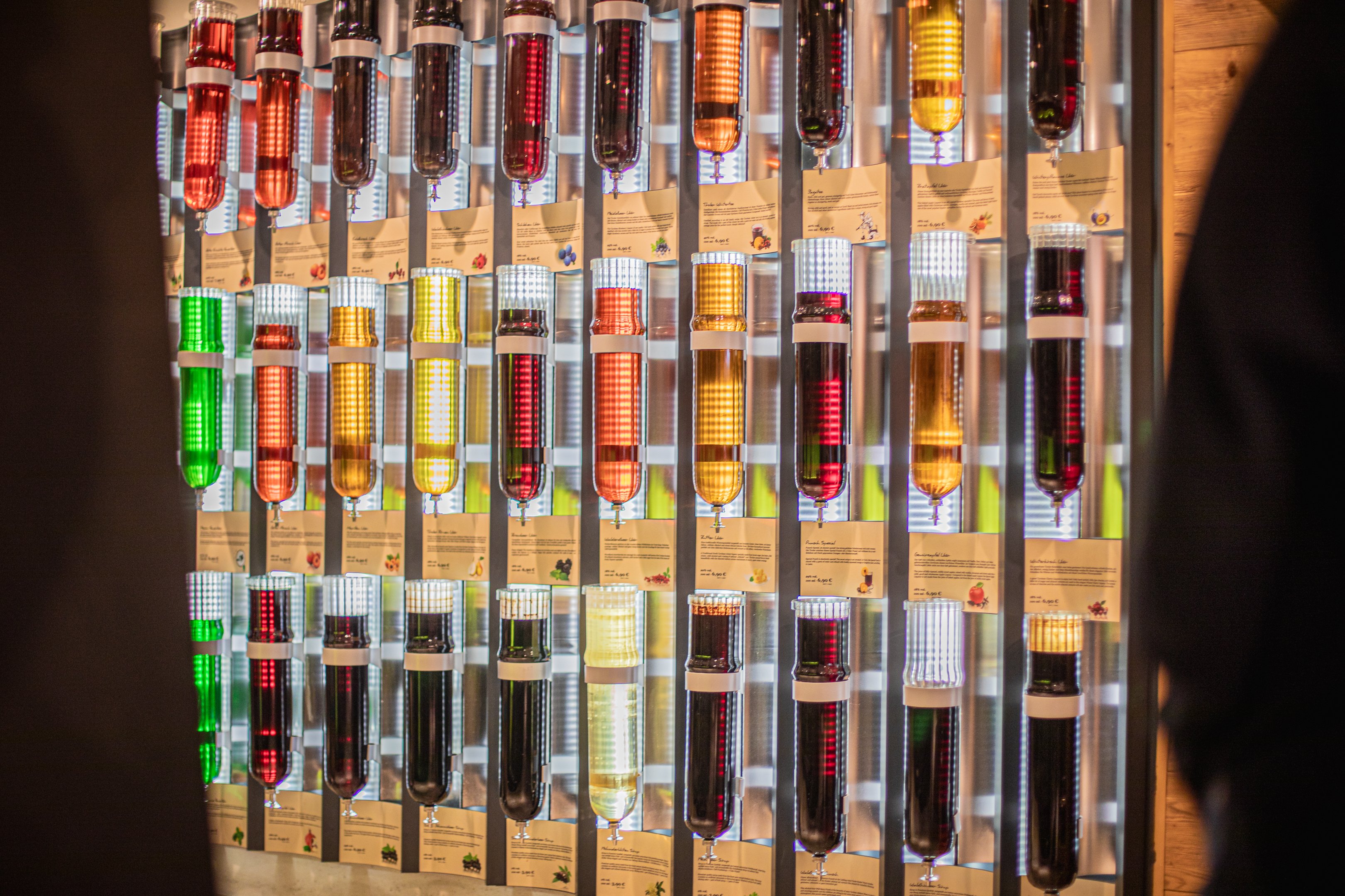 Una parete piena di bottiglie colorate di vetro con liquori e grappe.