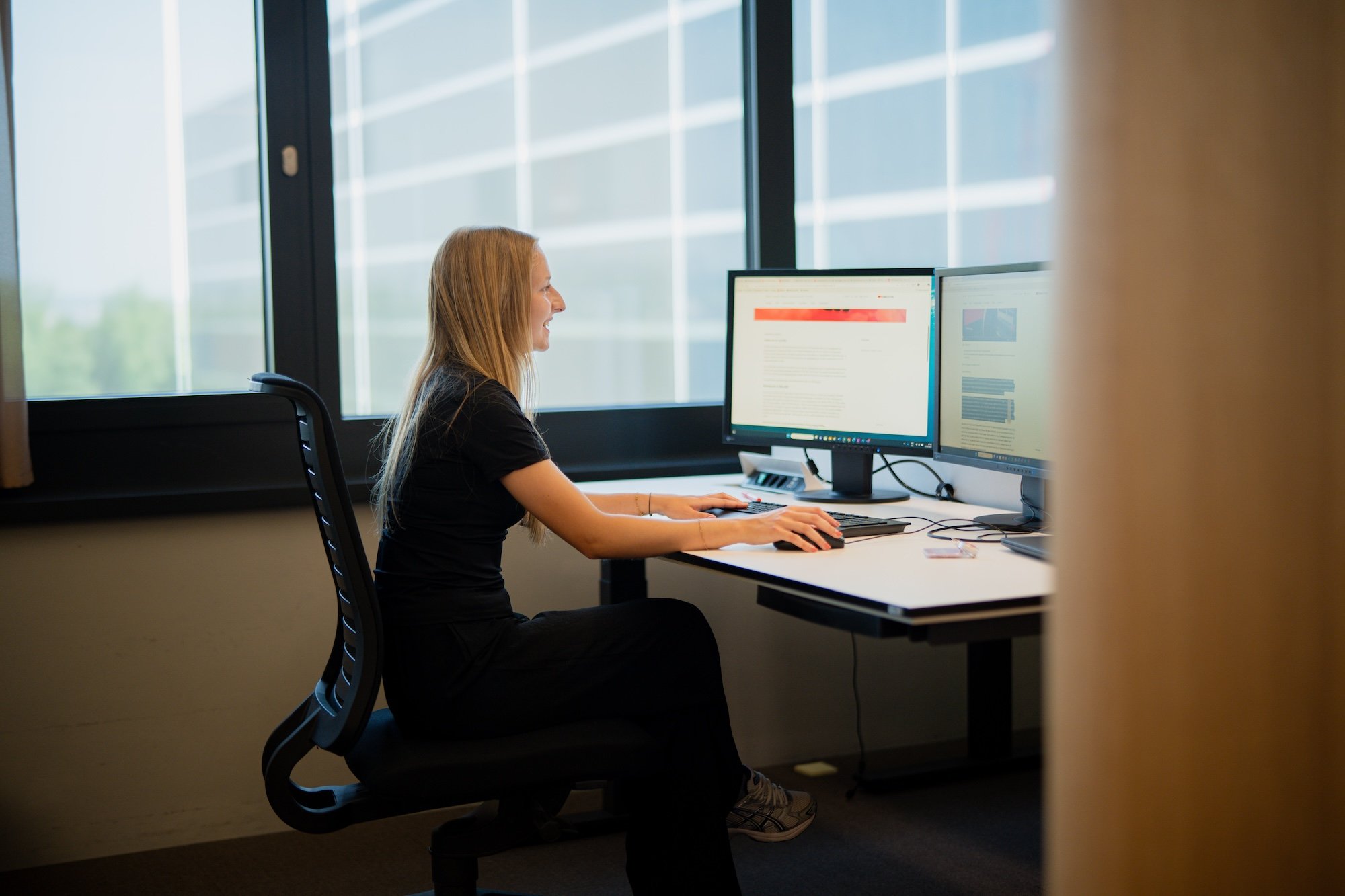 Una donna è seduta dietro una scrivania con due monitor.