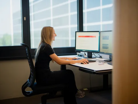 Una donna è seduta dietro una scrivania con due monitor.