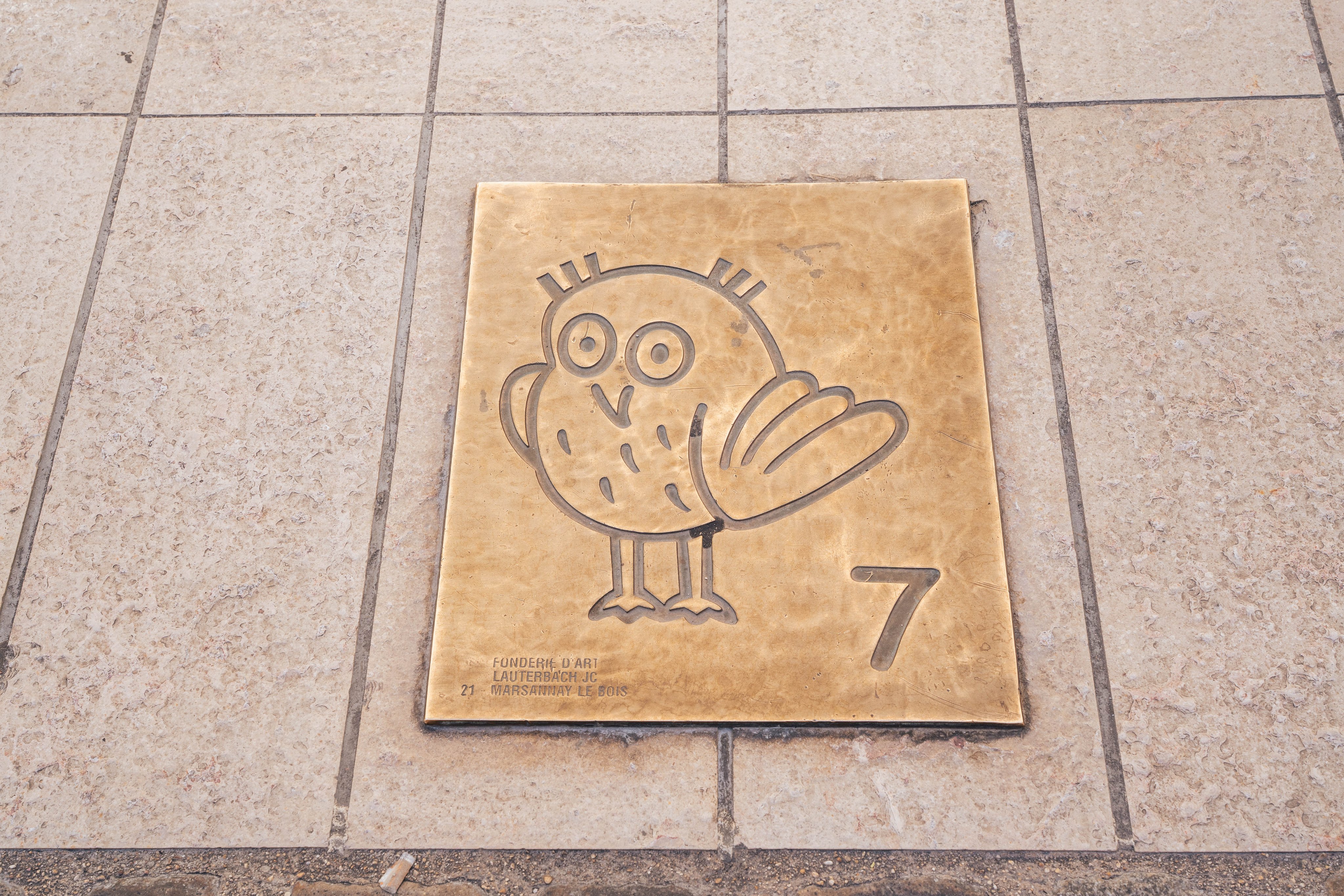 Una placca posizionata a terra, con una civetta e il numero sette incisi sul metallo. 
