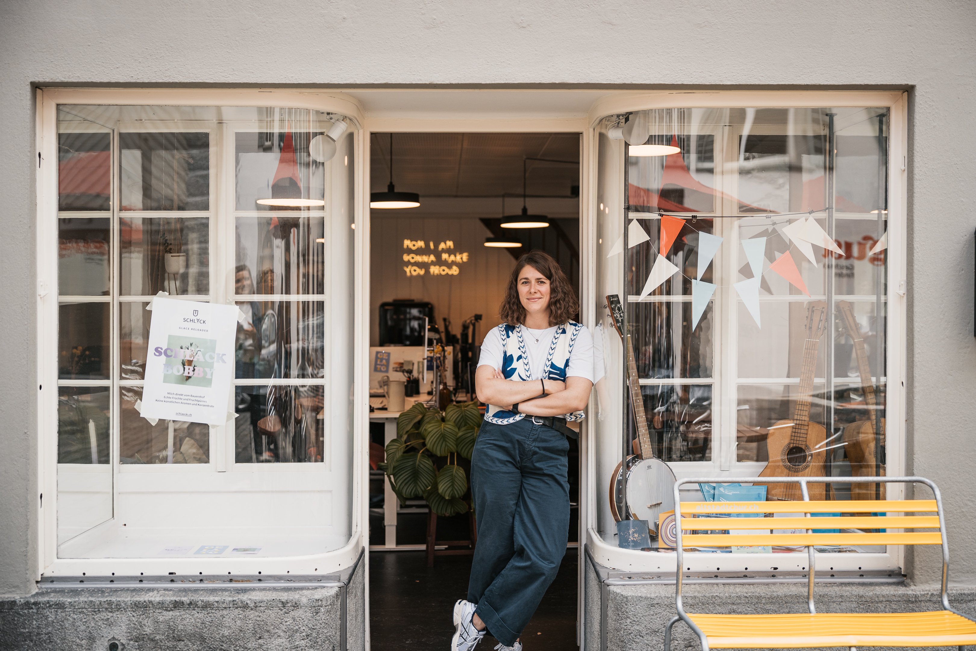 Sarah Schott in piedi davanti al proprio ufficio nel centro storico di Coira. A destra dell’ingresso si trova una panchina gialla.