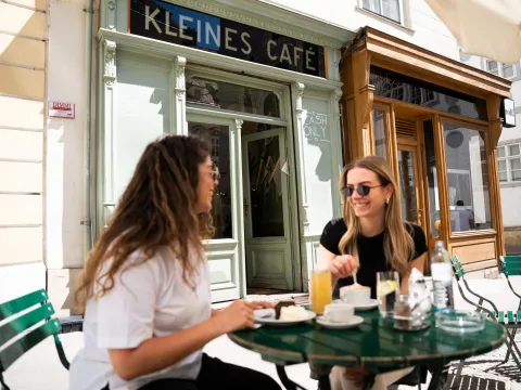 Due donne siedono al sole davanti a una caffè e una fetta di torta Sacher al Kleines Café di Franziskanerplatz a Vienna.