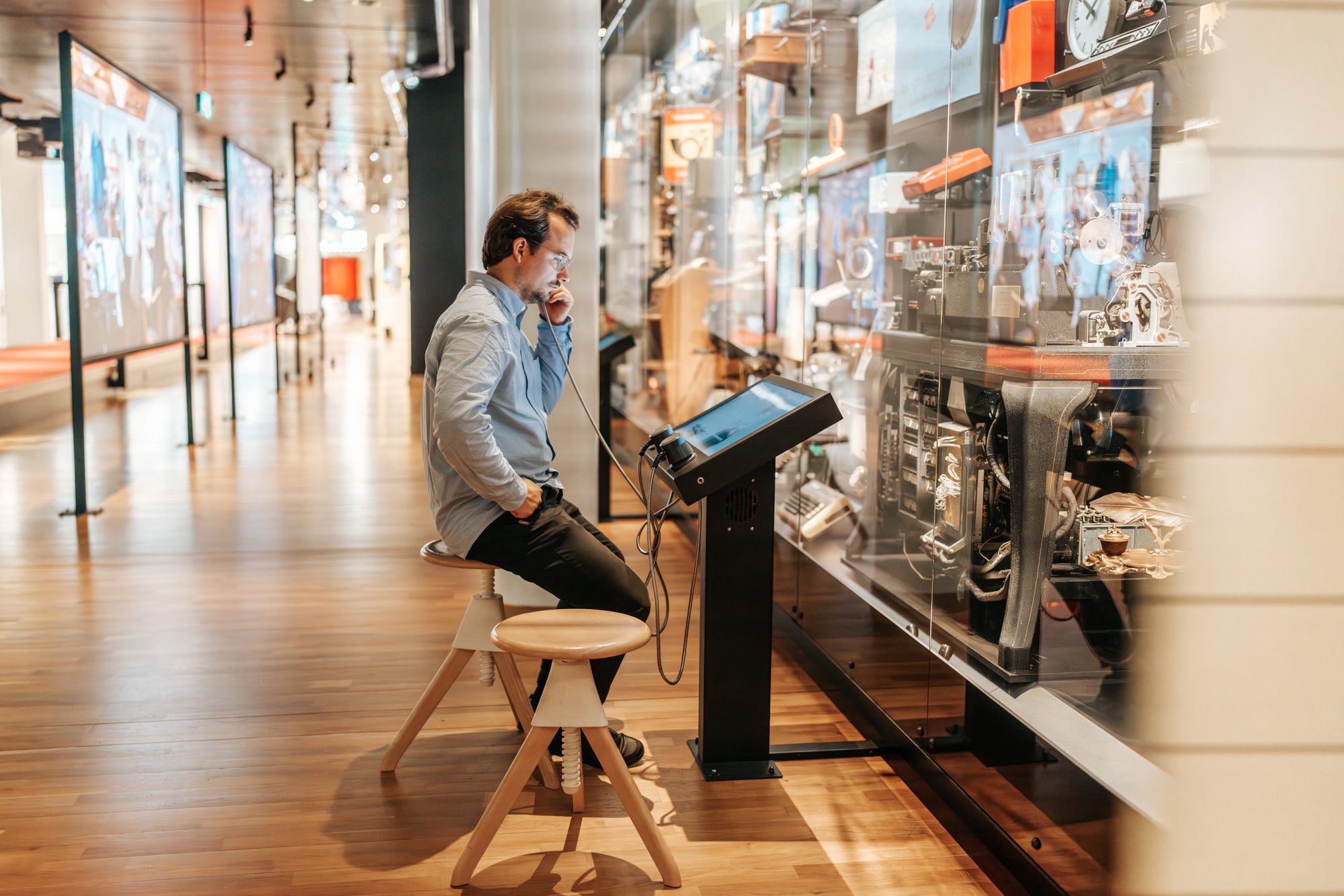 Mann sitzt im Museum und hört in einen altmodischen Hörer. 