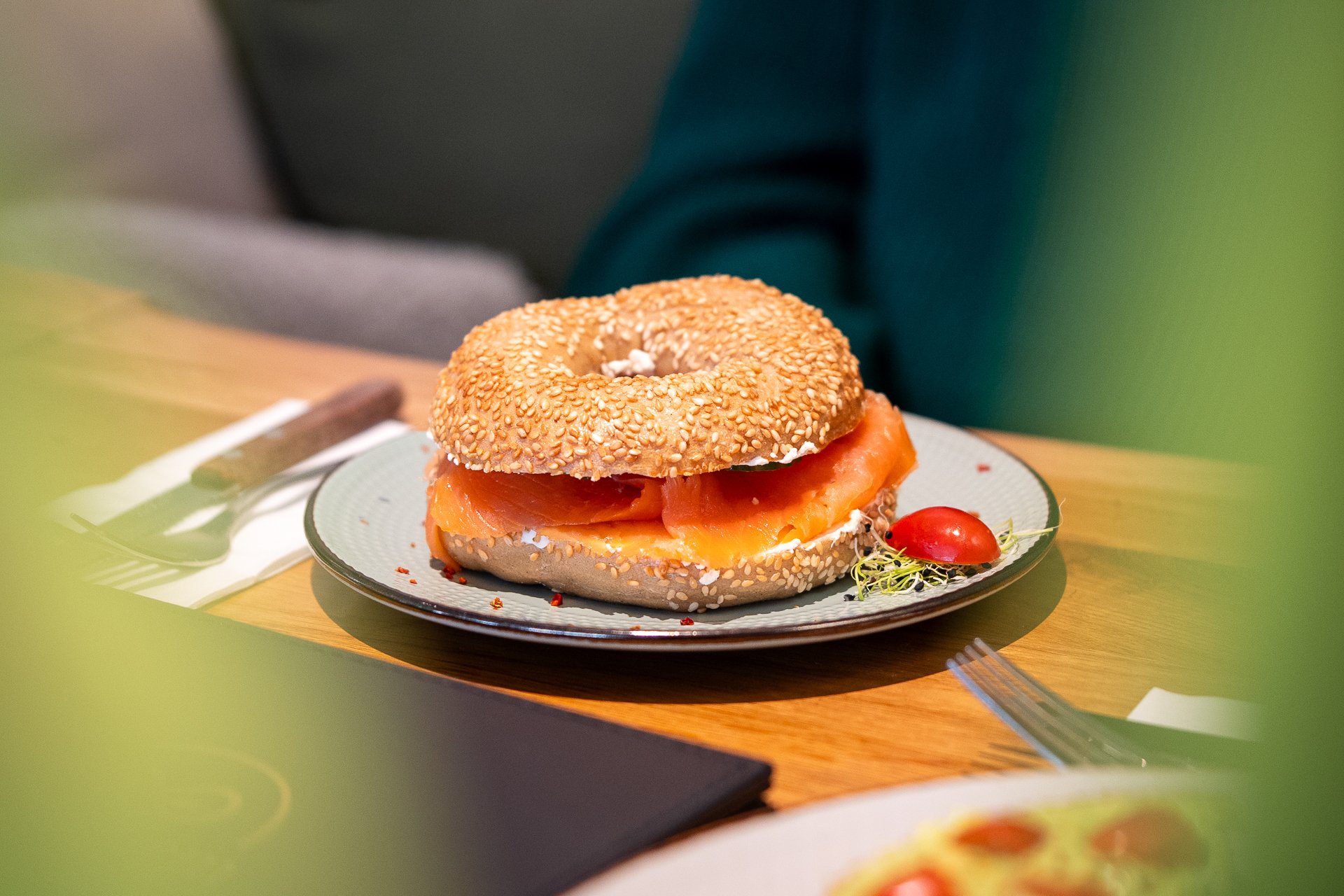 Auf einem Holztisch steht ein Teller, auf dem ein belegter Bagel liegt.