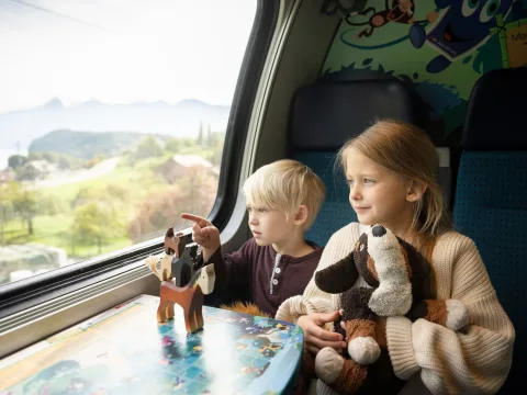 Zwei vergnügte Kinder malen im SBB Familienwagen. Sie sind auf dem Weg in den Europa-Park.