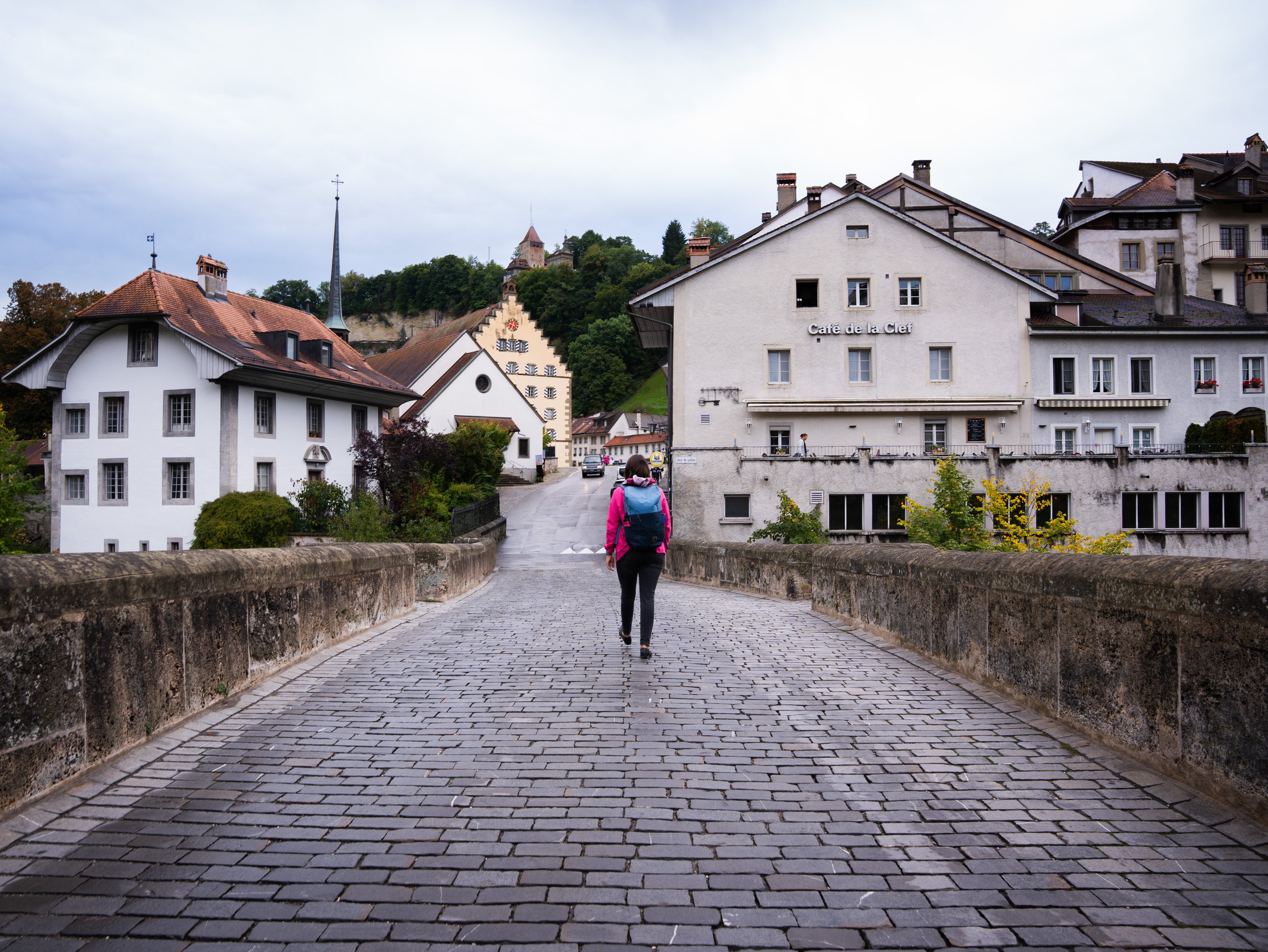 Une personne de dos dans une rue pavée; à l’arrière-plan, des maisons.