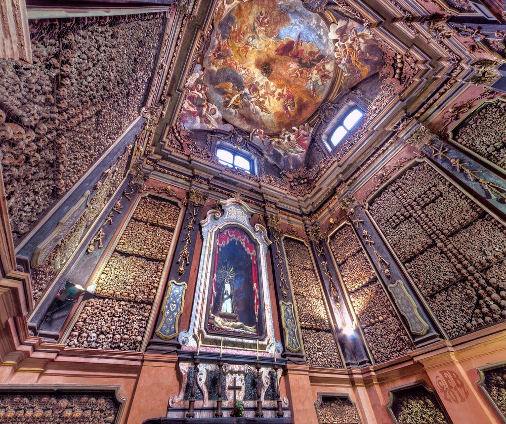 Una stanza con un altare, un dipinto sul soffitto e teschi e ossa umane alle pareti.