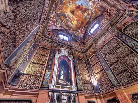 Una stanza con un altare, un dipinto sul soffitto e teschi e ossa umane alle pareti.