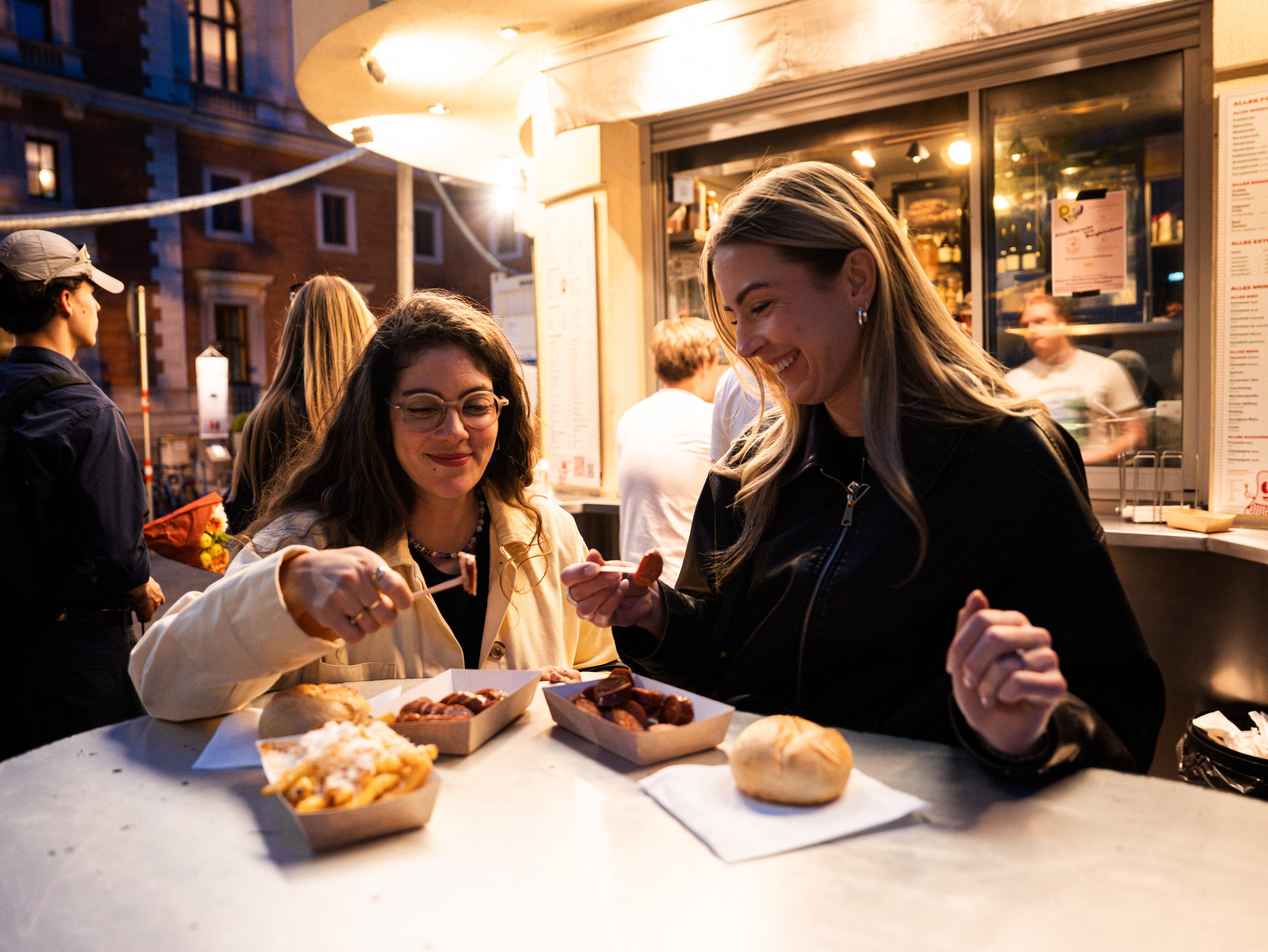 Due donne cenano con käsekrainer e patatine al chiosco di salsicce Alles Wurscht di Vienna.