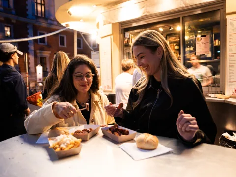 Due donne cenano con käsekrainer e patatine al chiosco di salsicce Alles Wurscht di Vienna.