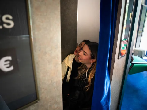 Due donne siedono al buio dietro a una tenda blu in una cabina per fototessere nel 25hours Hotel di Vienna.