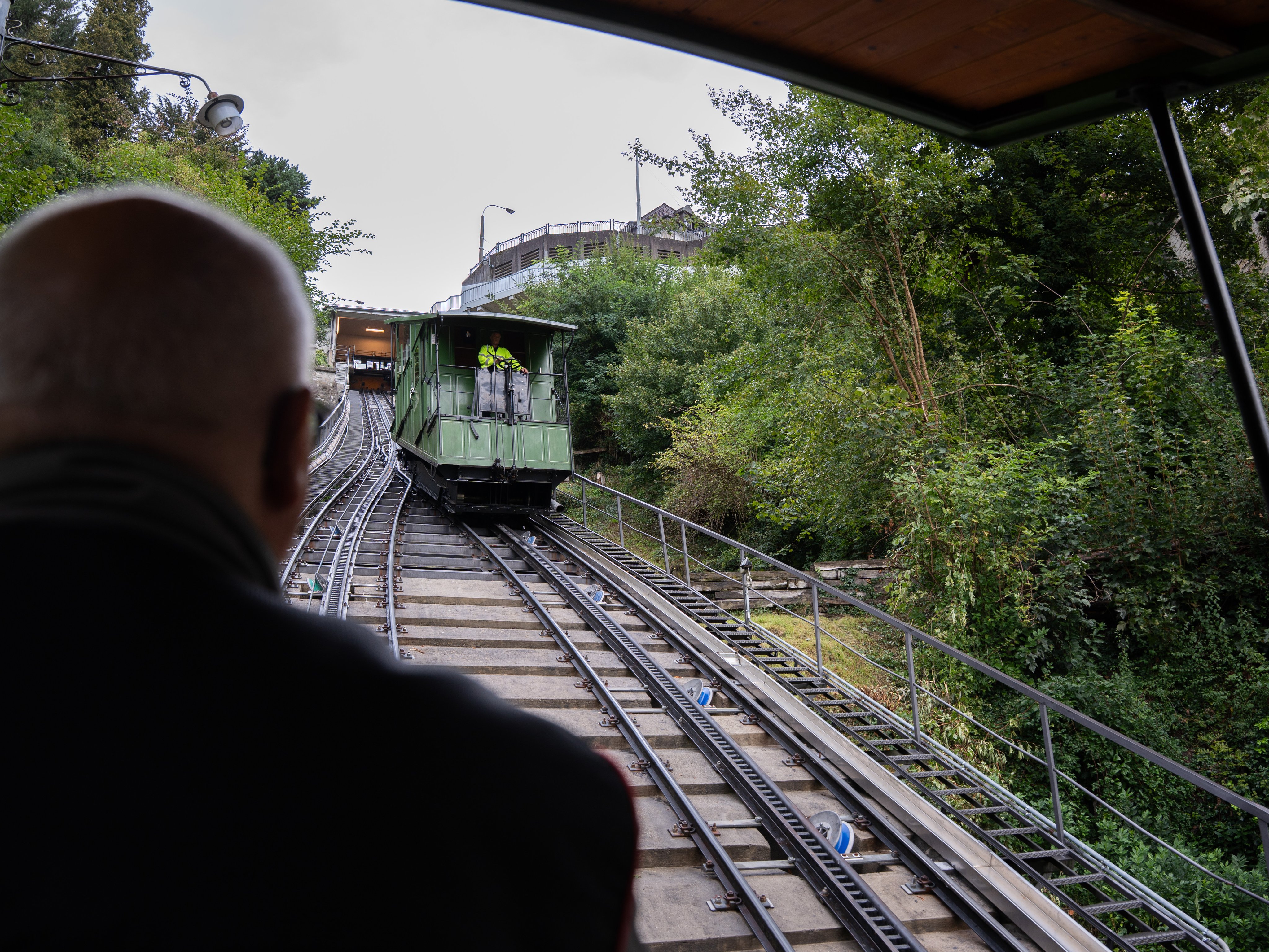 Un homme vu de dos et des rails qui montent abruptement. Sur les voies circule une petite cabine verte.