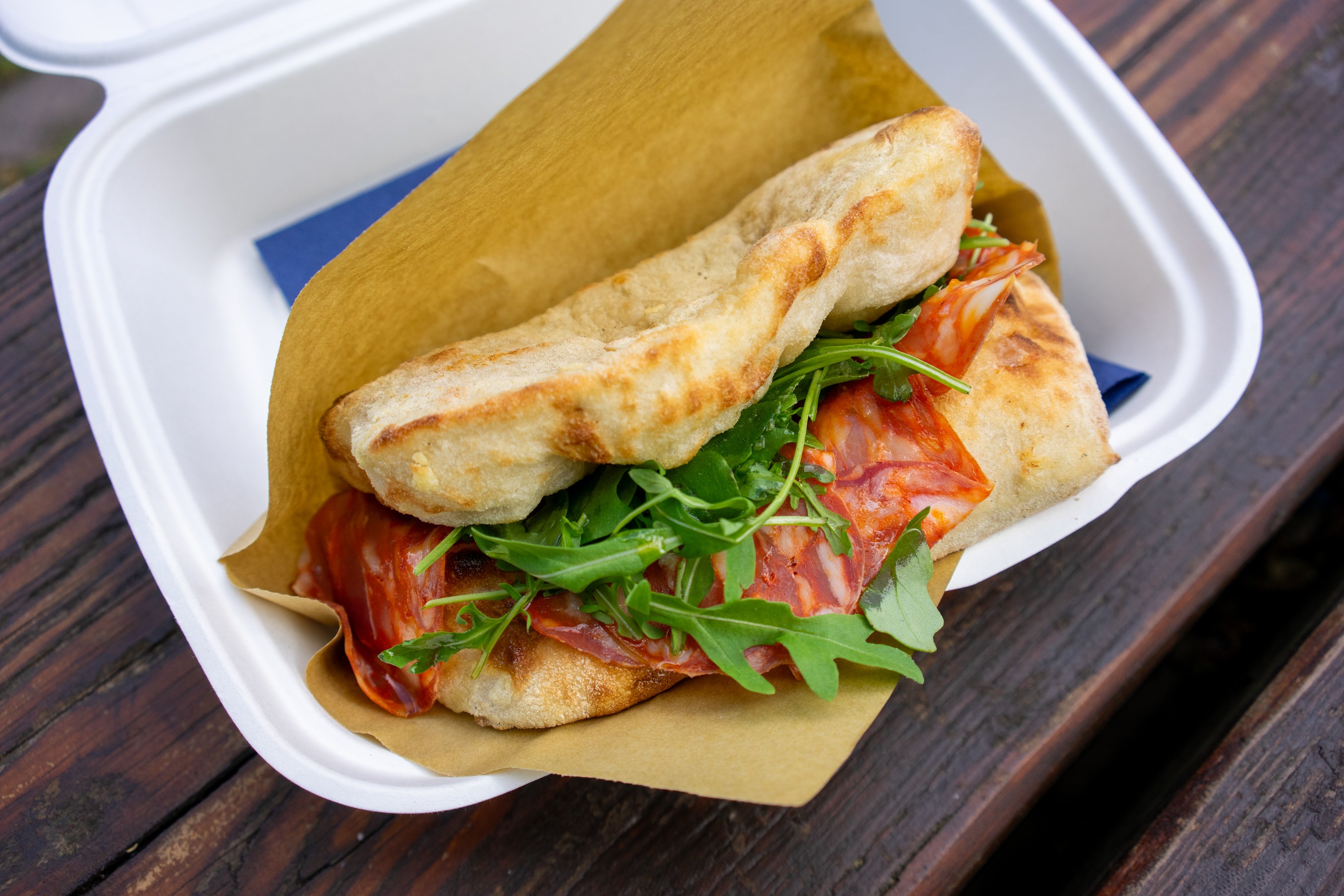 Ein Sandwich mit Salami und Rucola in einer weissen Take-Away Box.