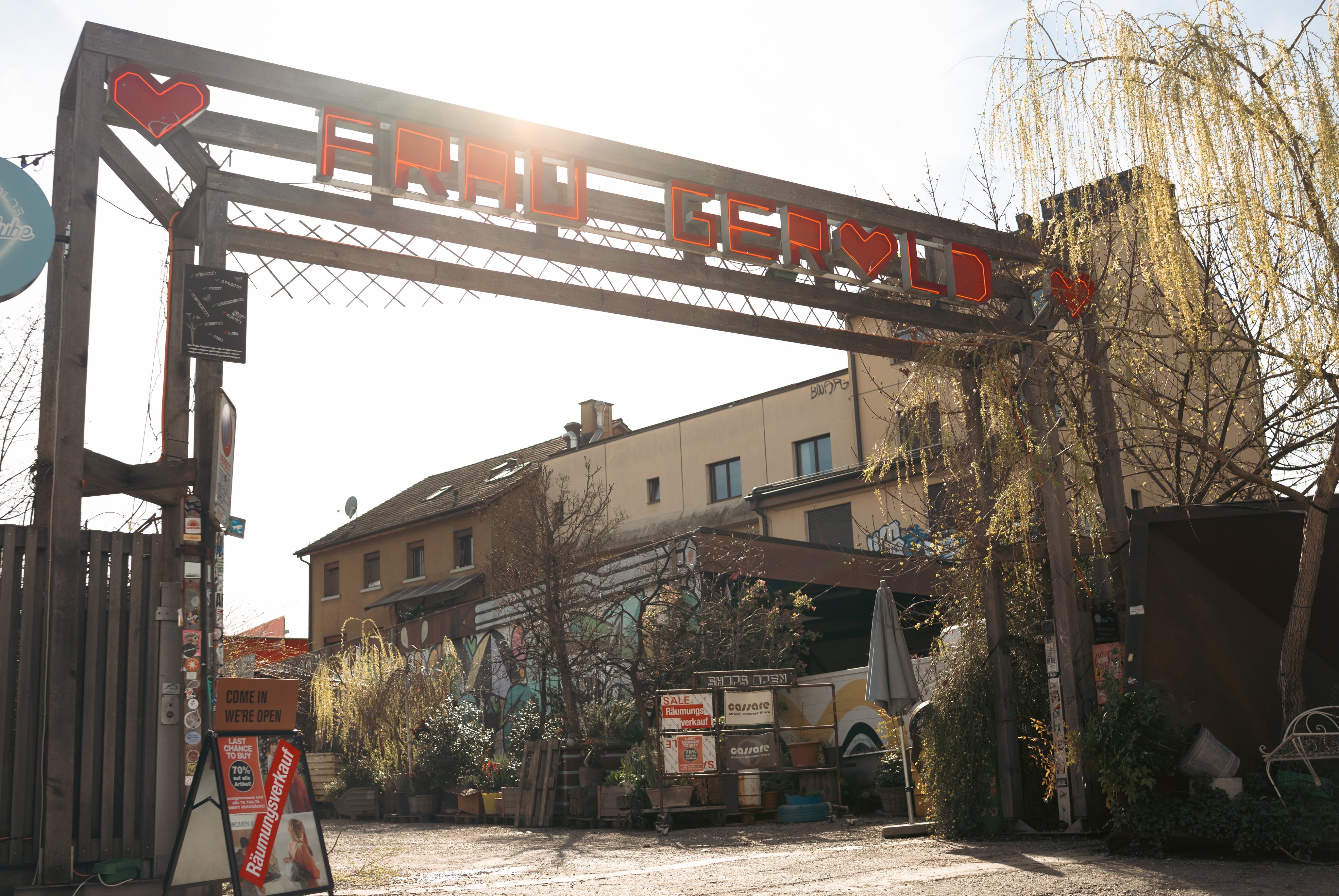 Un grand portail en bois marque l’entrée sur un site hétérogène et artistique. L’inscription «Frau Gerold» figure en rouge sur l’arc du portail.  