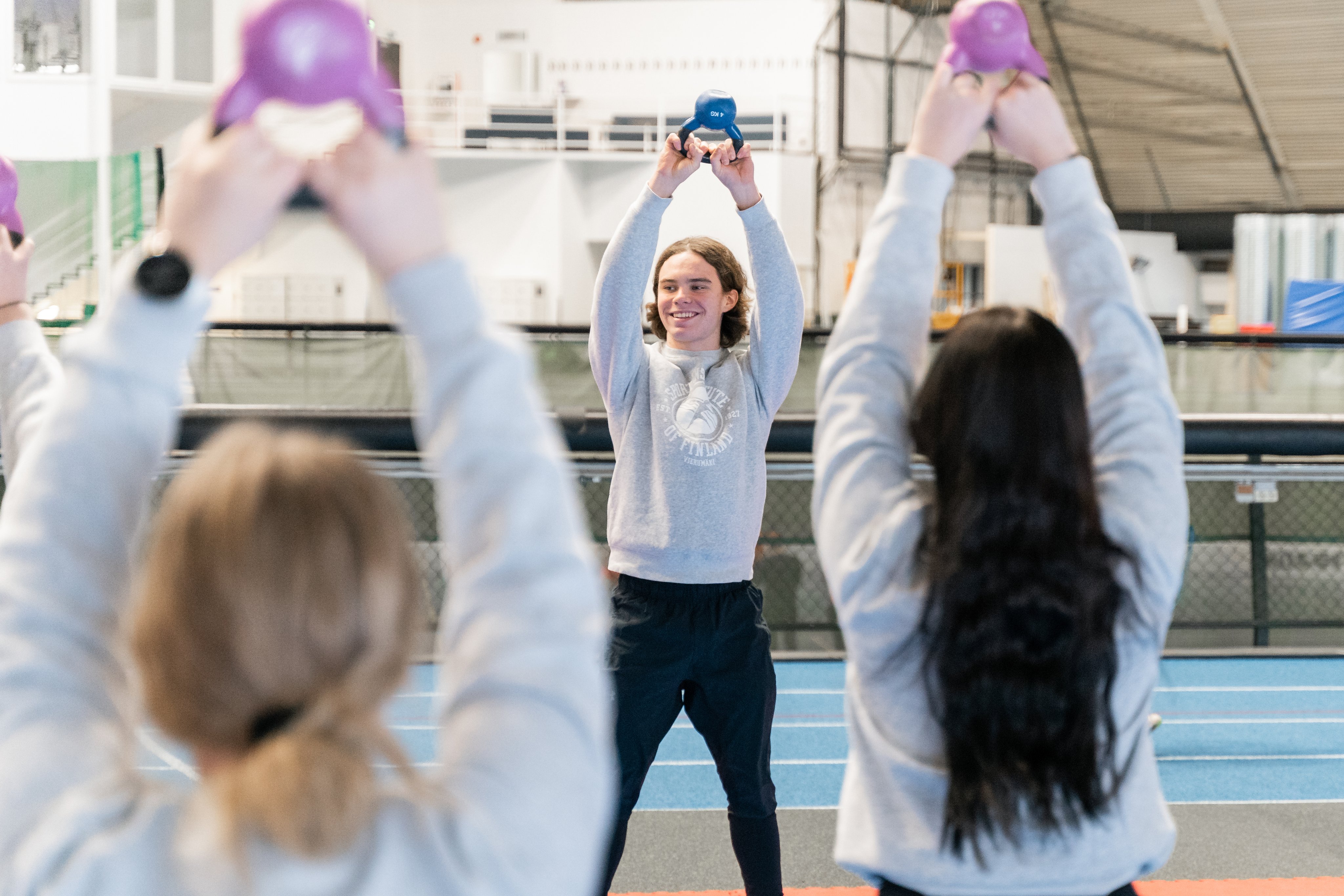 Ohjaaja kahvakuula kädessä ja kaksi asiakasta hänen edessään.