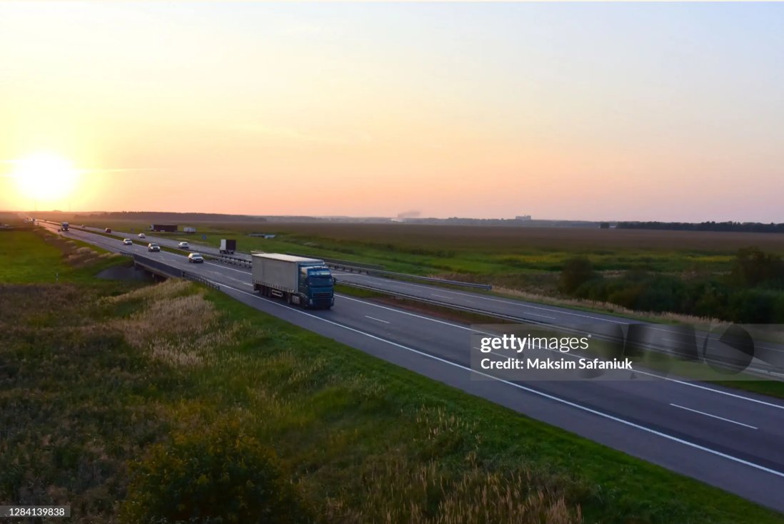 Väg genom landskap kantad av träd och en sjö
