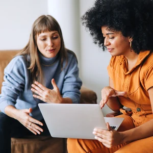 Kaksi henkilöä istuu sohvilla läppärin kanssa.