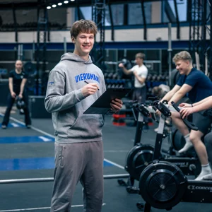 Ohjaaja kuntosalilla. Kaksi ihmistä pyöräilee vieressä.