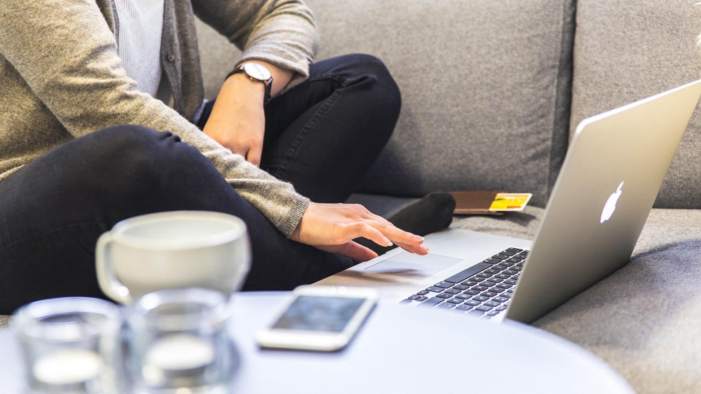 Sohvalla läppäri ja sitä käyttävä henkilö