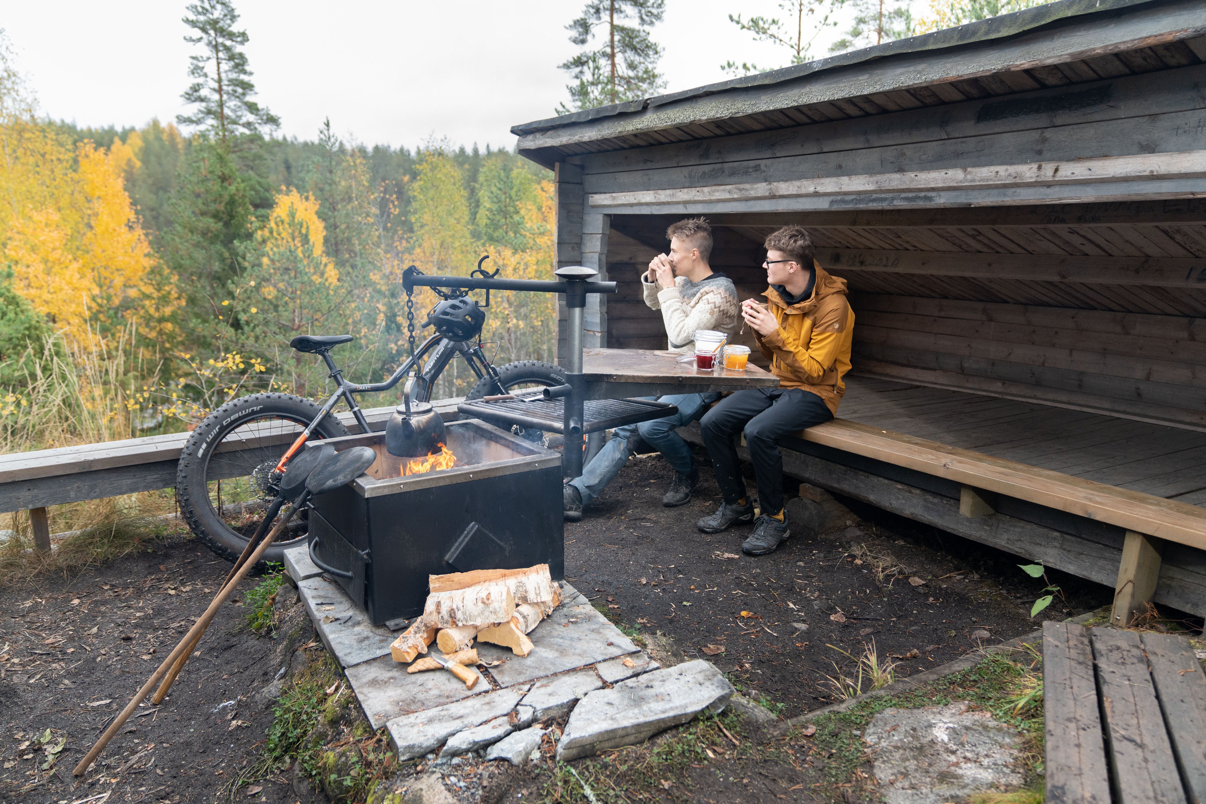 Kaksi miestä istuu laavulla nuotion äärellä.