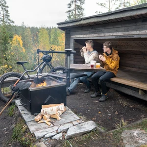 Kaksi miestä istuu laavulla nuotion äärellä.