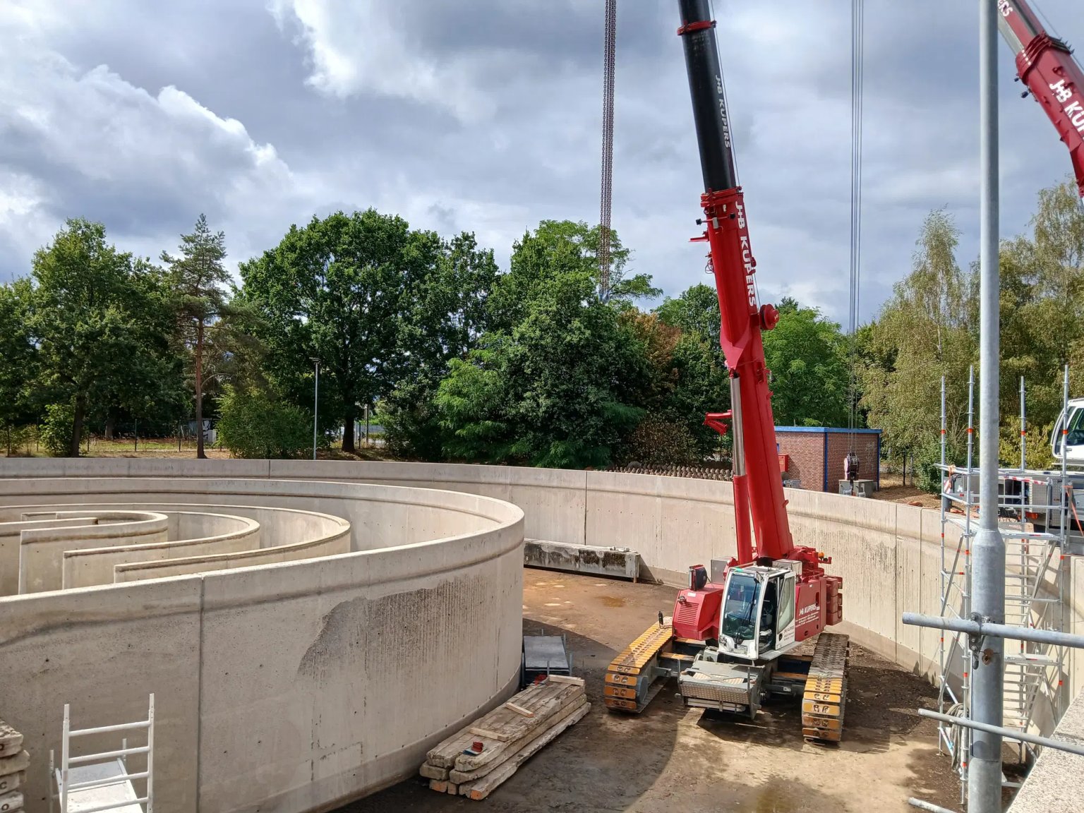 Baumgarten mit Kränelementen und Baugerüsten auf einer Baustelle, im Hintergrund Bäume
