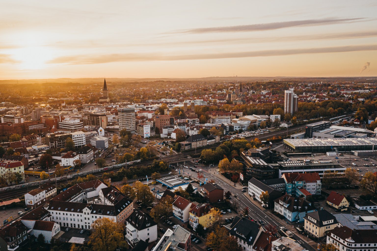 Luftaufnahme einer Stadt bei Sonnenuntergang mit Gebäuden, Straßen und Bäumen