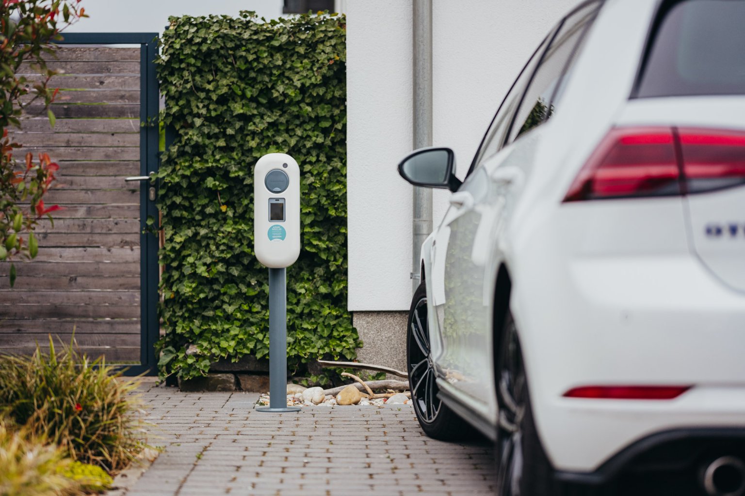 E-Ladebox vor Einfamilienhaus. Daneben steht ein Elektroauto.