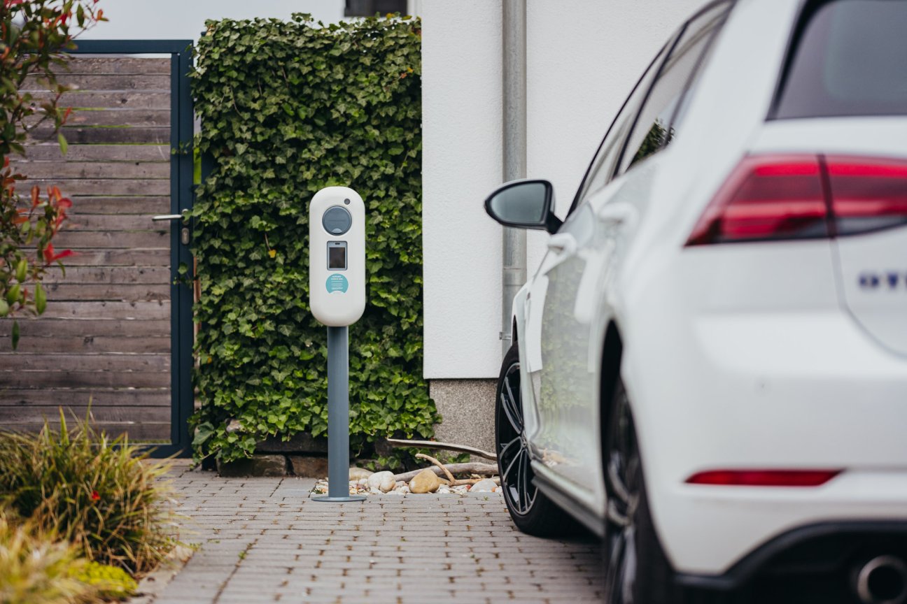 E-Ladebox vor Einfamilienhaus. Daneben steht ein Elektroauto.