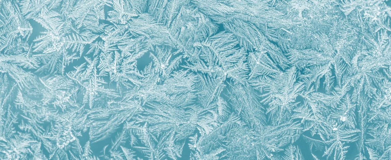 Nahaufnahme feiner Eiskristalle auf einer gefrorenen Oberfläche in hellen Blau- und Weißtönen.