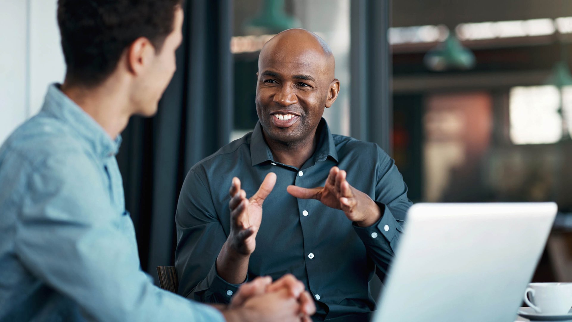 A cheerful business professional collaborates with a colleague on marketing ideas using a laptop in a modern office