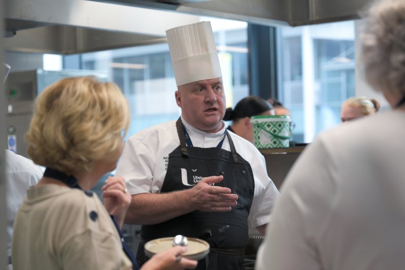 Culinary instructor mentoring students in the Academy Restaurant professional training kitchen.