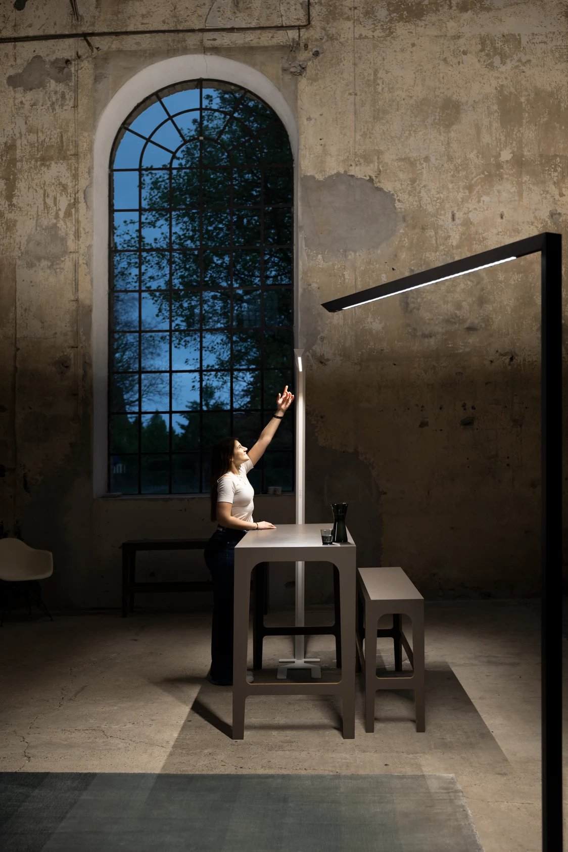 One person and two Skena table lamps in a tall industrial space that gains a modern architectural vibe from the luminaire. 