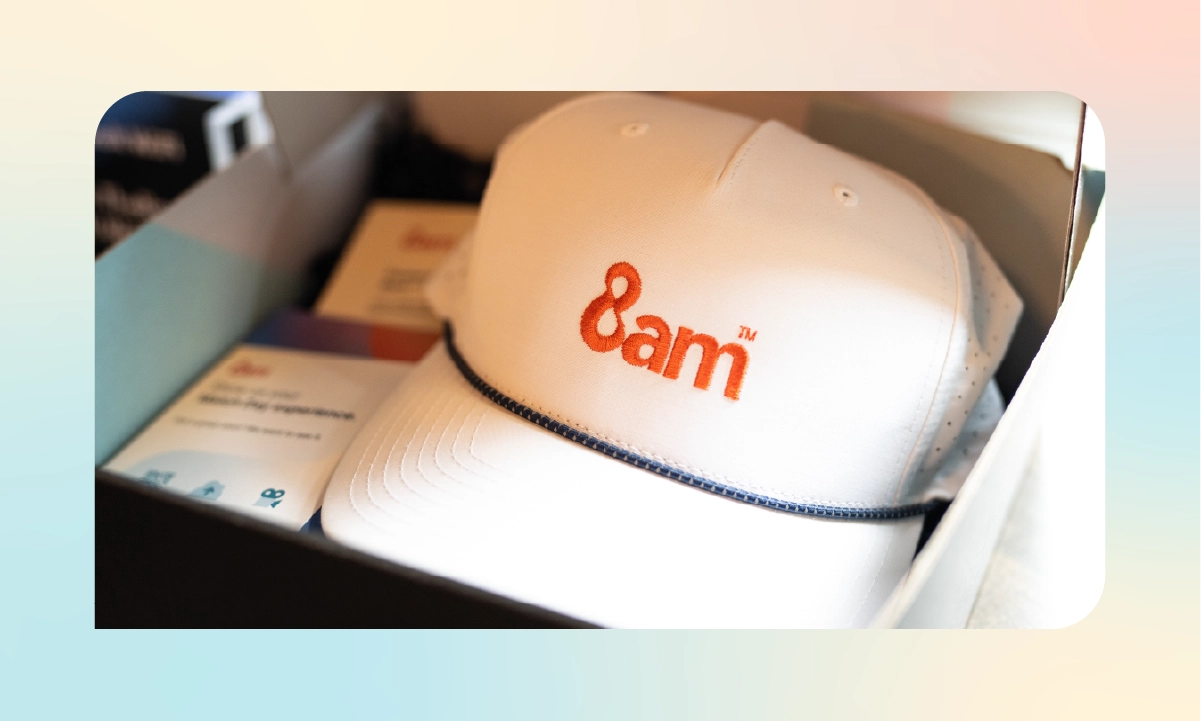 A white 8am-branded cap displayed inside an attendee gift box.