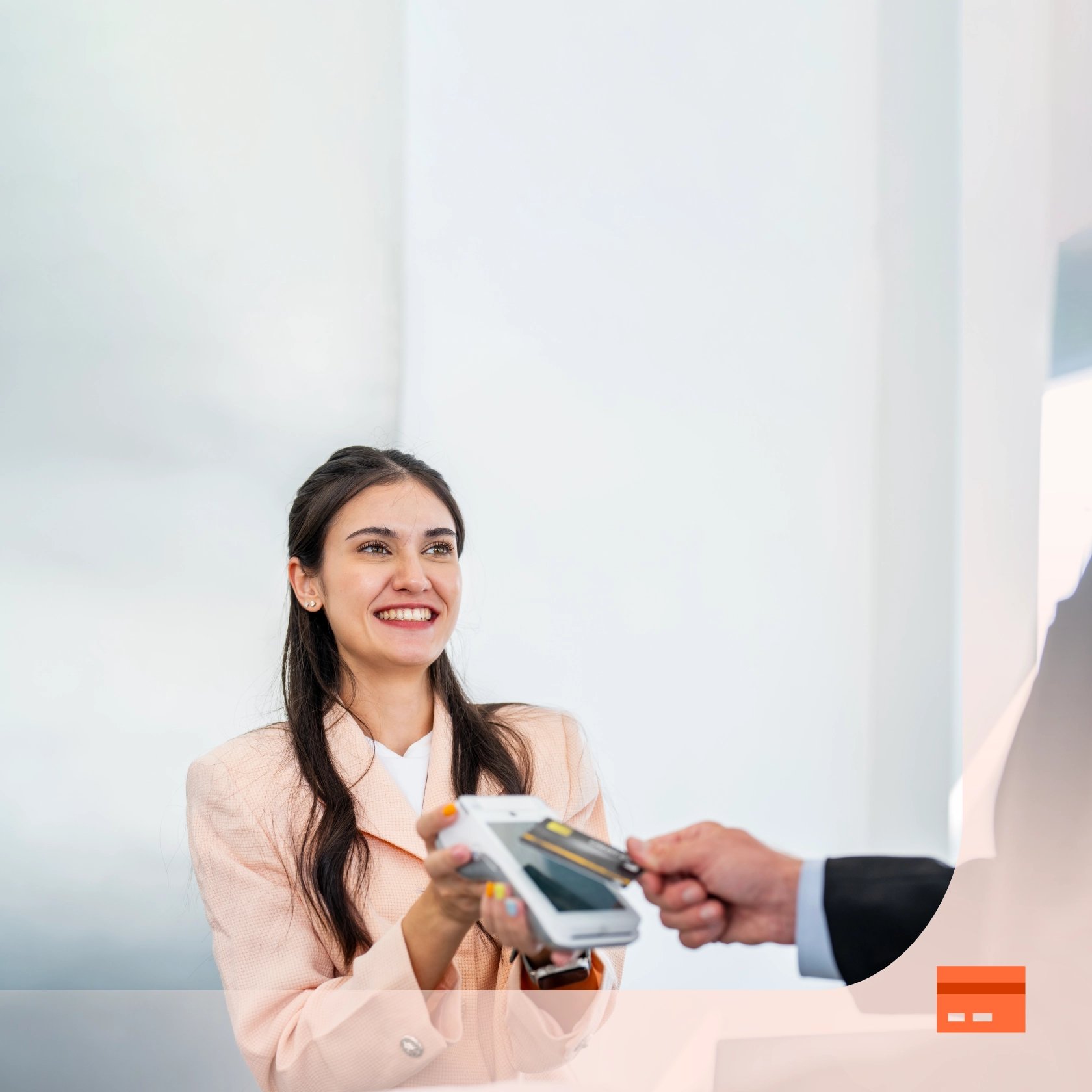 A smiling woman in business attire holds a payment terminal as a person in a suit taps a smartphone to make a contactless payment.