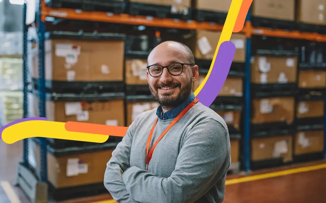 Hombre sonriente con gafas en una bodega, frente a estanterías con cajas que importó gracias a la guía de comercio internacional.