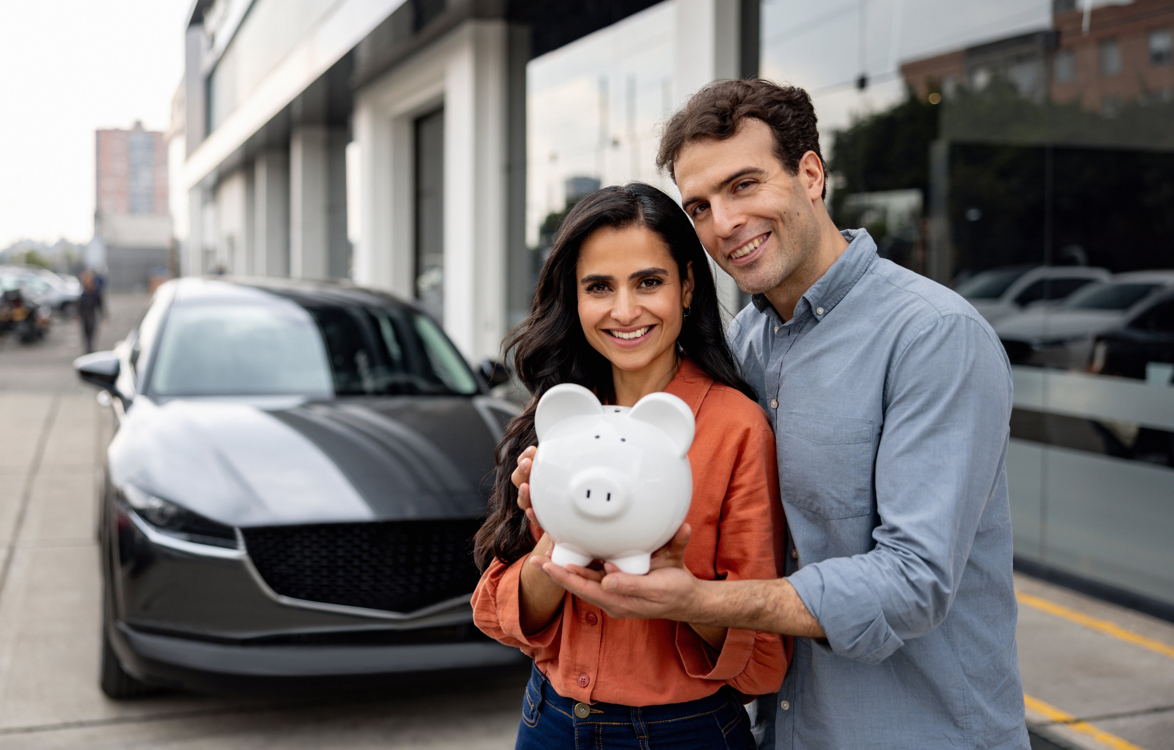 Portrait of a happy couple holding a piggy bank after buying auto insurance in front of their car.