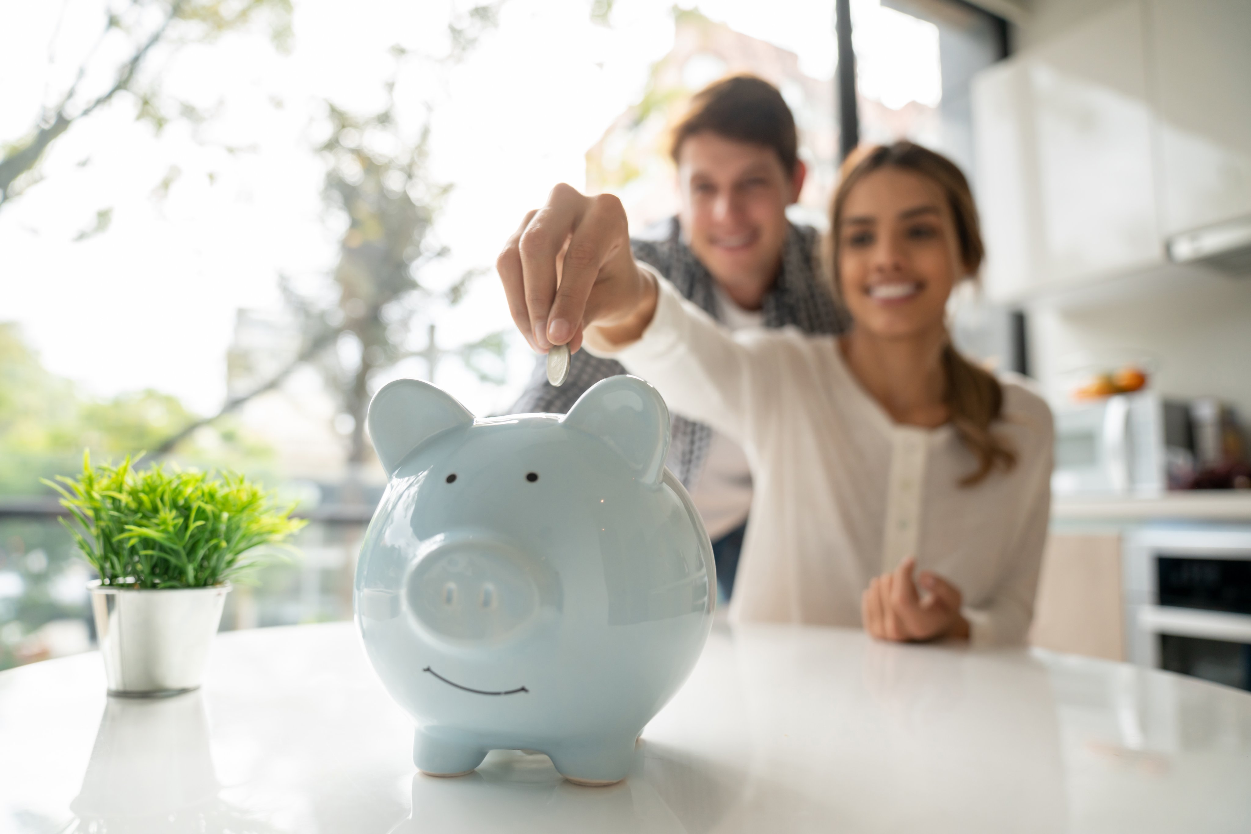 Focus on foreground of latin american young couple saving coins into piggy bank.