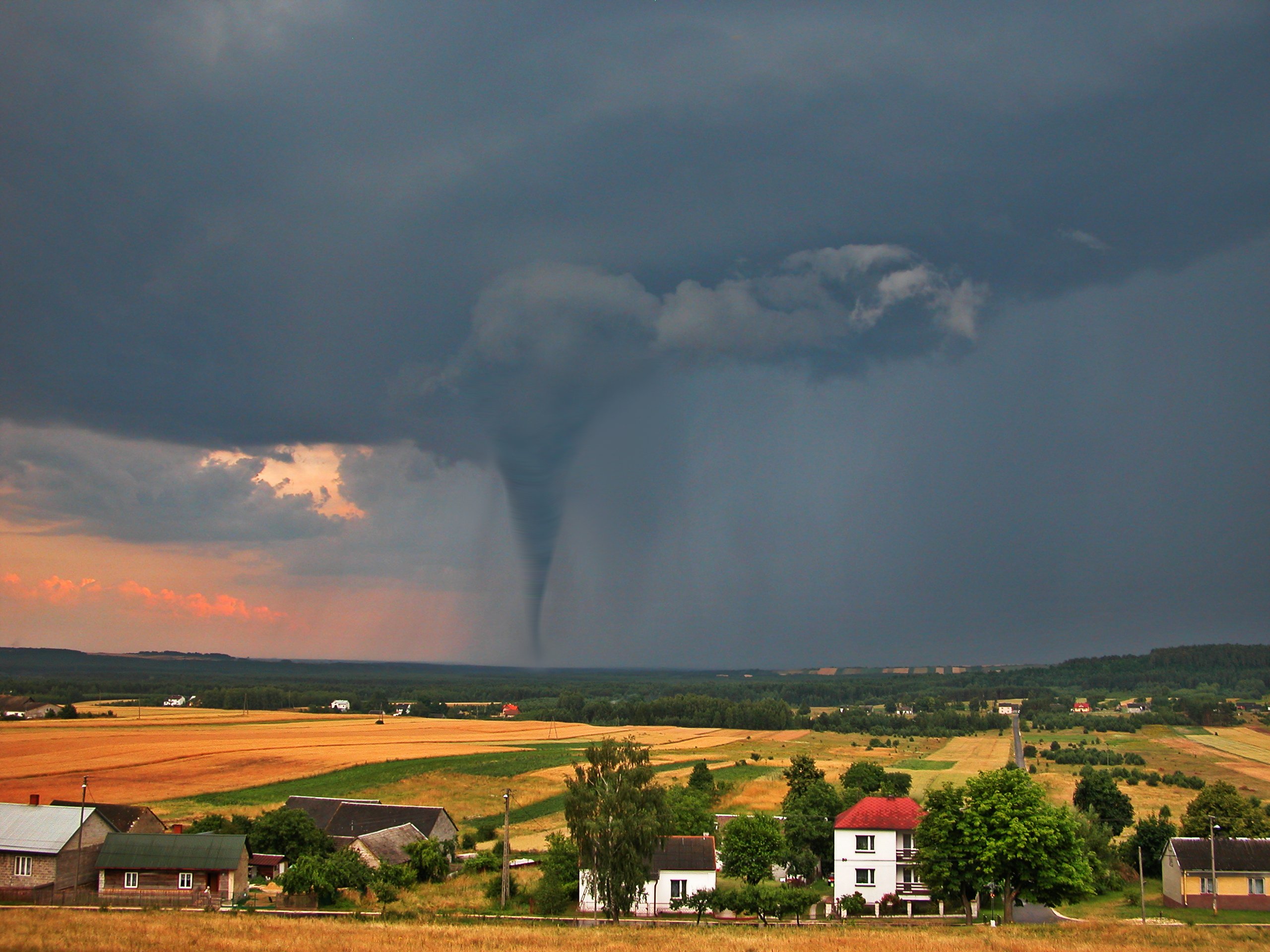  View of the serene countryside and stormy sky with a tornado in the background