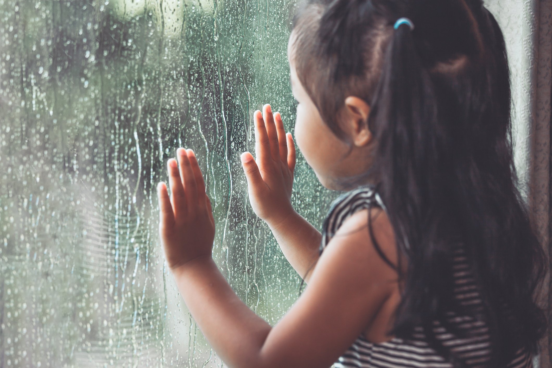 Young girl looking outside through a window on a rainy day