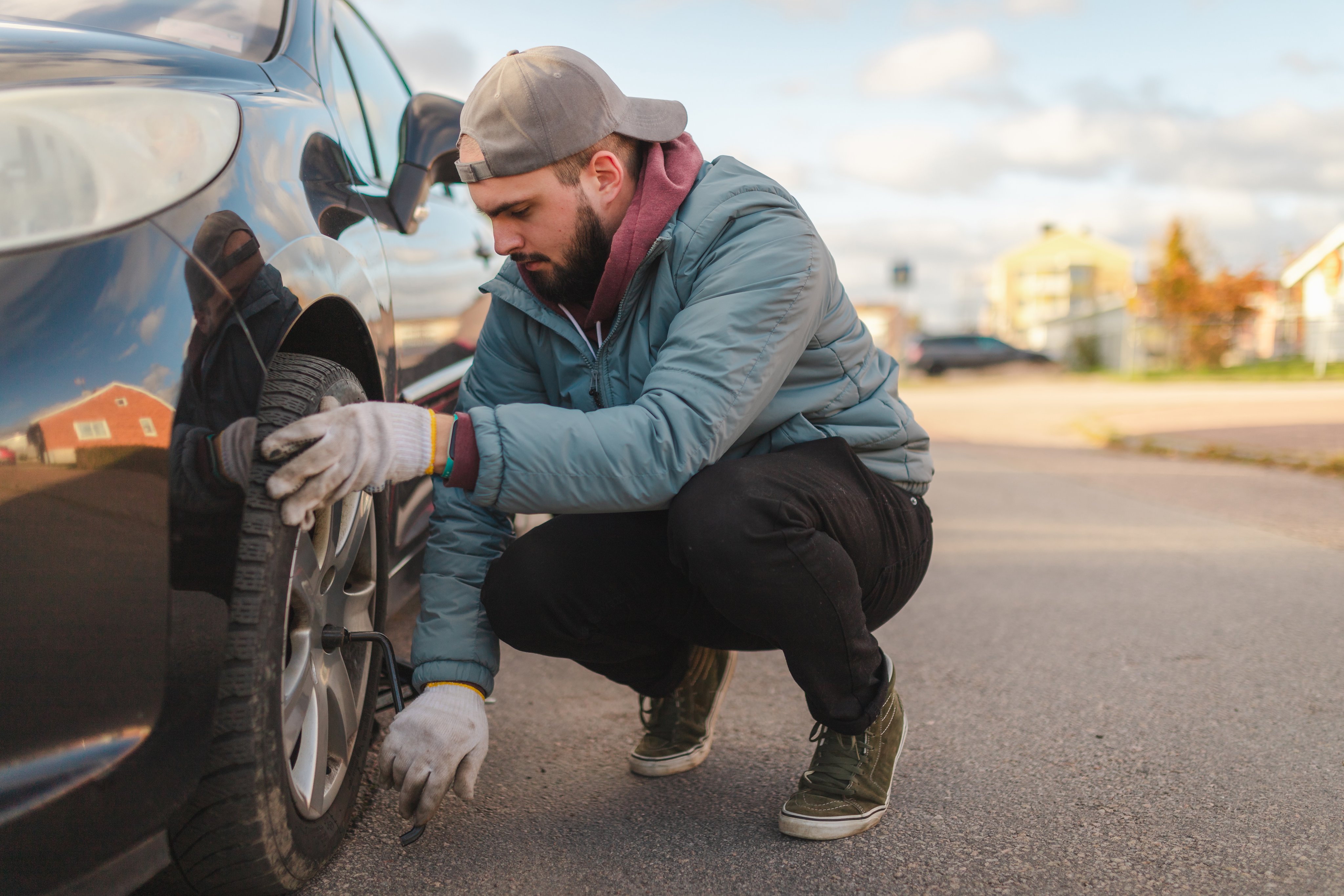Young man removing the tire from his car before replacing it with a winter tire. Preparing for winter